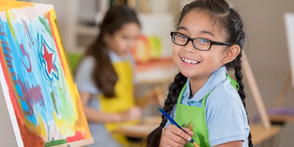 Beautiful Filipino elementary age art student smiles while working on a painting in art class.