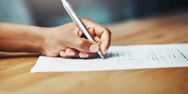 Cropped shot of a woman filling in some paperwork at a desk